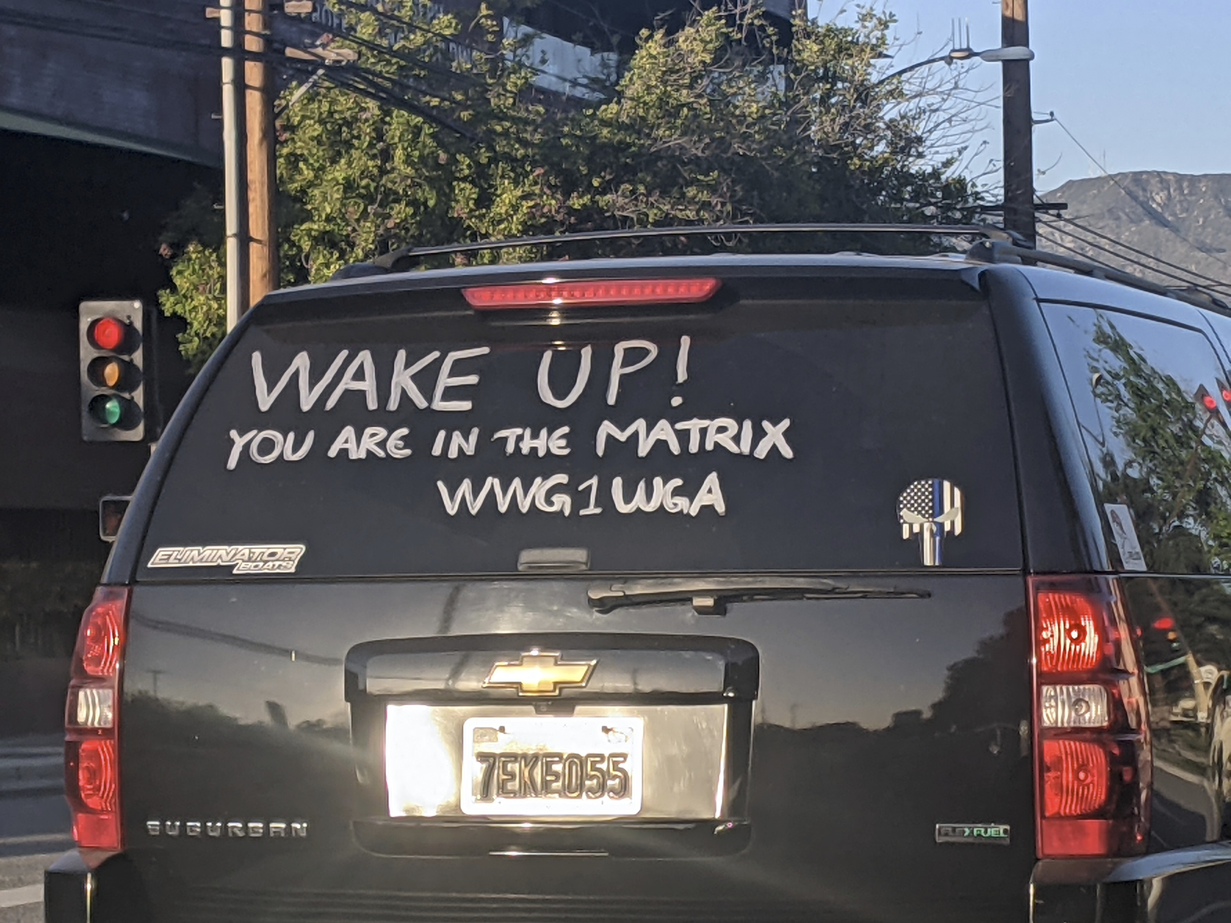 Photo showing a car with the text "WAKE UP! YOU ARE IN THE MATRIX WWG1WGA" painted on the back windshield along with a thin blue line Punisher logo, all representative of the online conspiracy theory QAnon